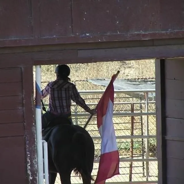 Mariya on horseback carrying the flag, seen through a barn doorway