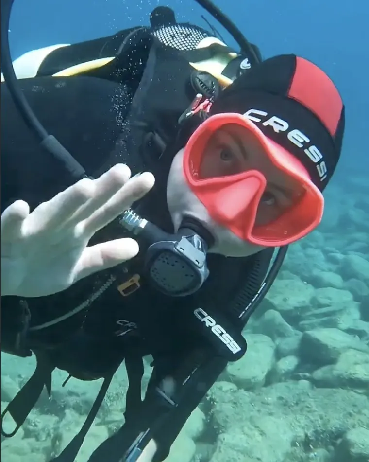 Mariya waving at the camera underwater in a red mask