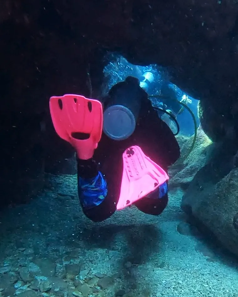 Mariya finning through a dark swim-through in pink fins
