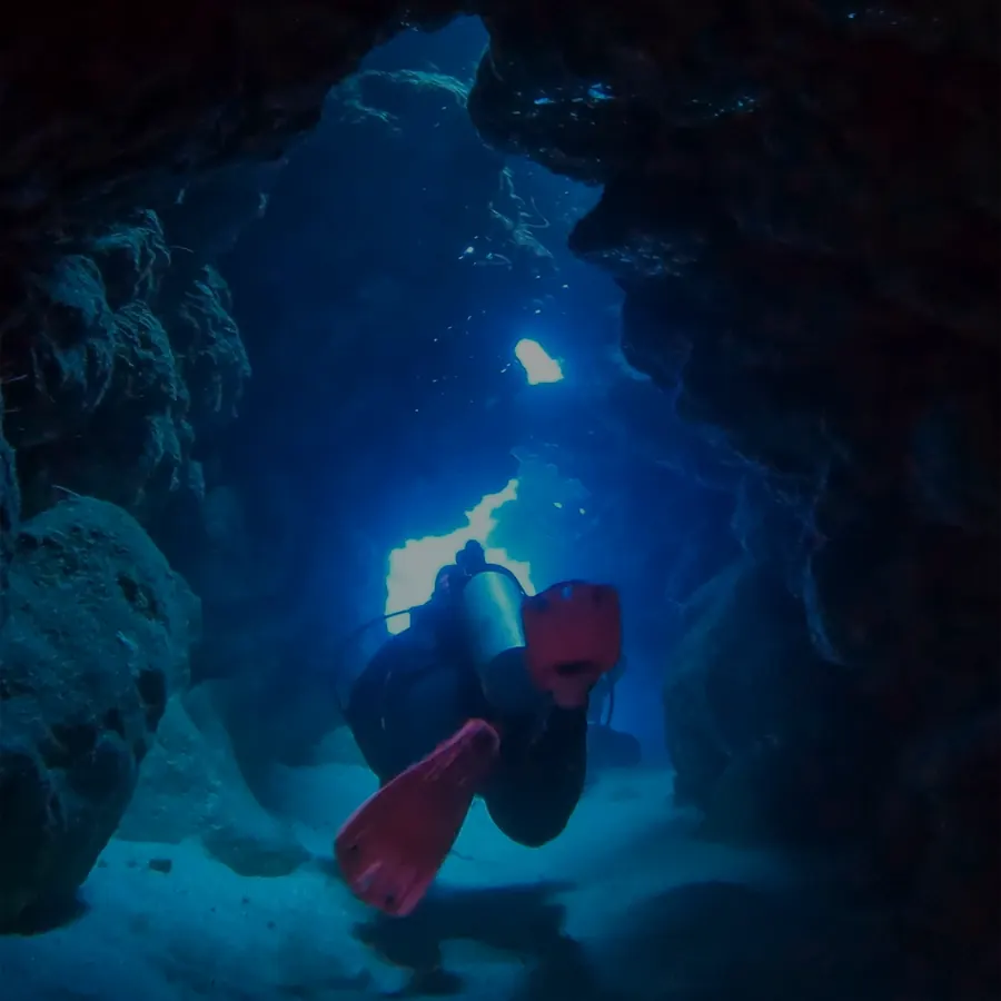 Mariya in pink fins swimming through a lit underwater tunnel