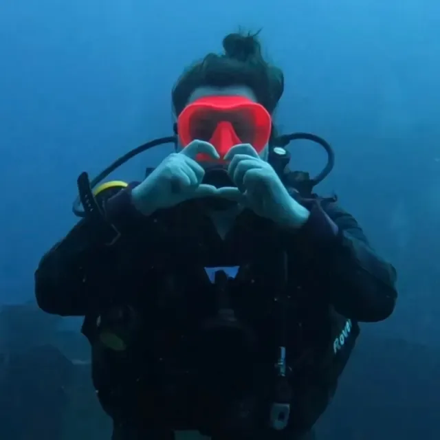 Mariya making a heart with her hands underwater in a red mask