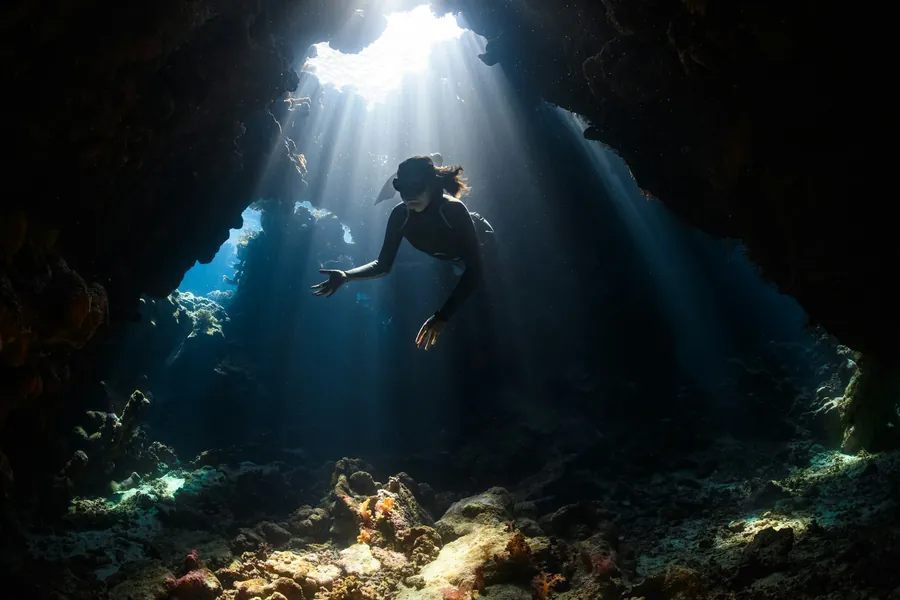 A diver in an underwater cave lit by sunbeams