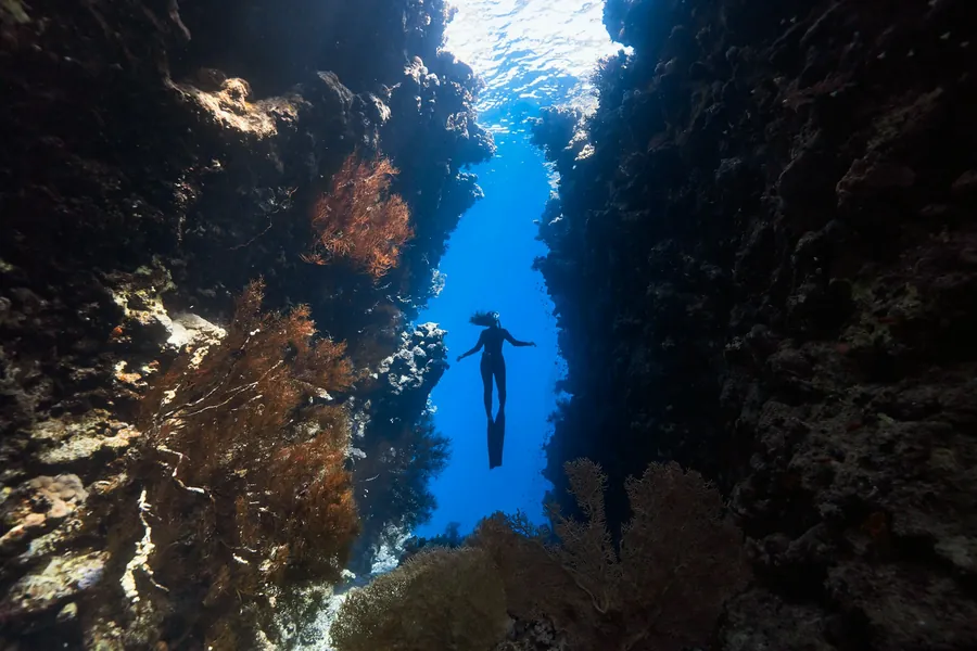 A diver swimming through a narrow underwater passage