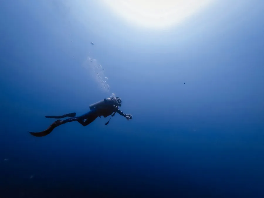 A scuba diver in deep blue water under a burst of sunlight