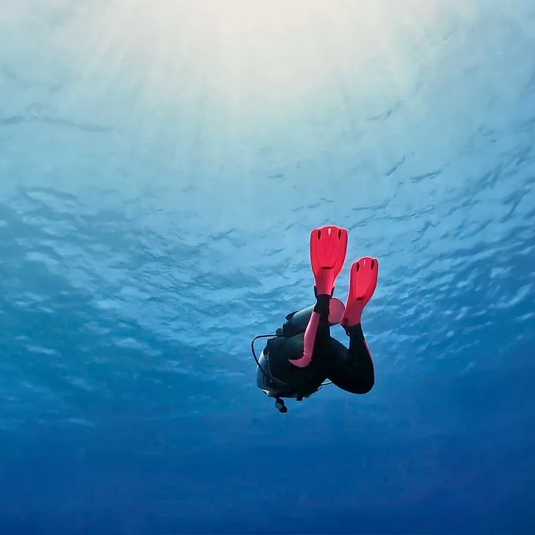 A diver dropping away from the lit surface into open blue