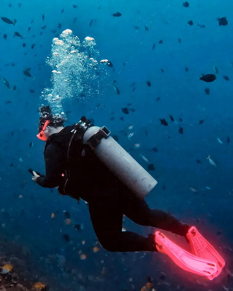 Mariya swimming out over the reef, trailing bubbles