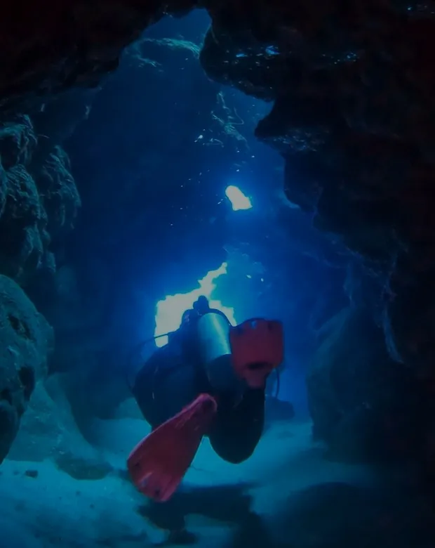 A diver in a swim-through, lit from the far end